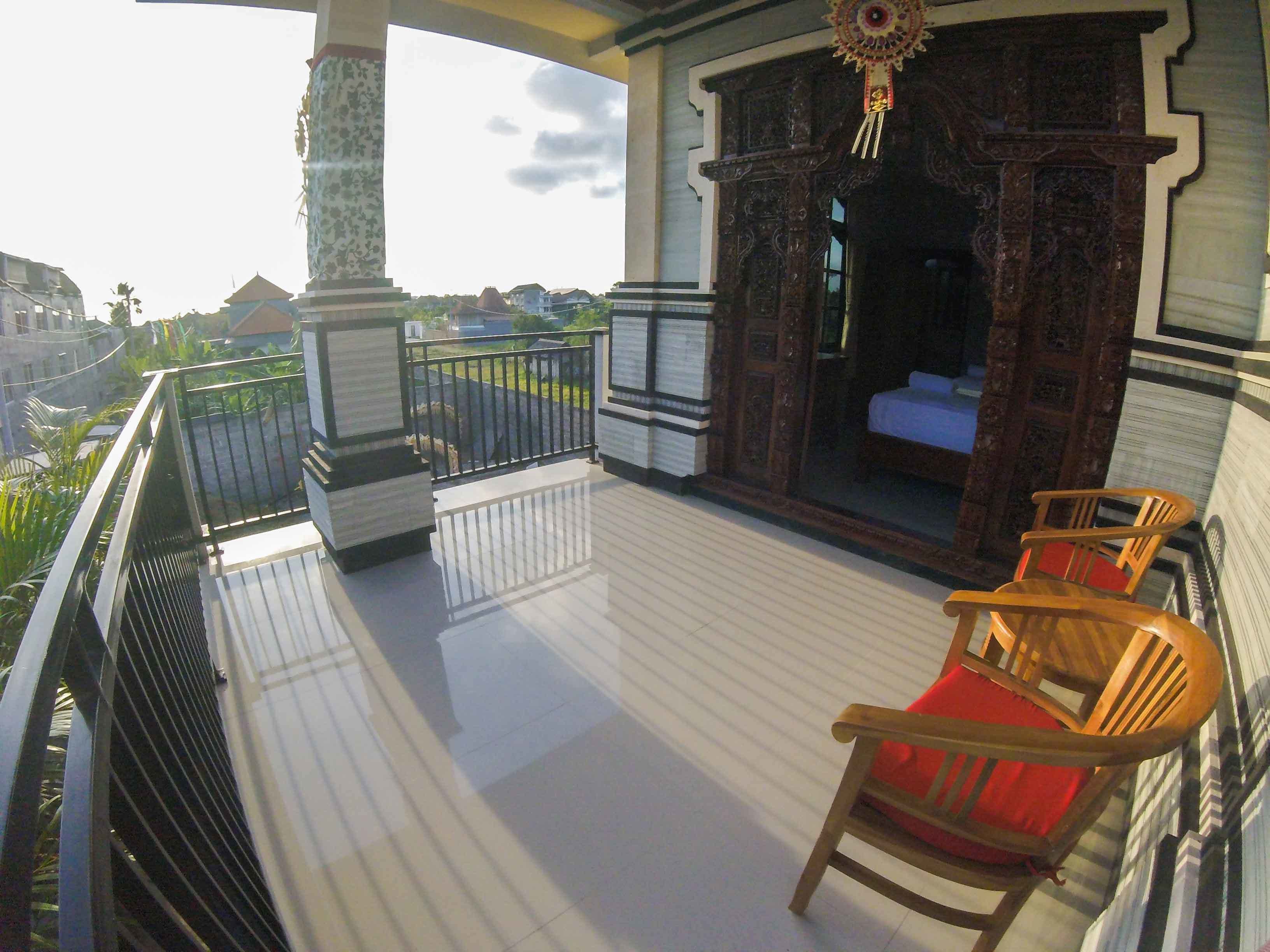 A balcony with a wooden floor, a railing, and two wooden chairs with red cushions.