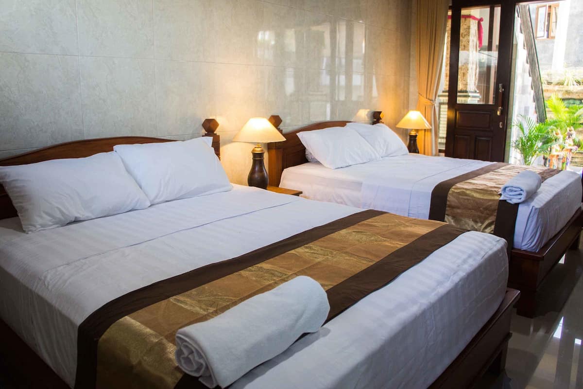 Hotellihuone, jossa on kaksi sänkyä. Kummassakin sängyssä on valkoiset vuodevaatteet ja ruskea koristetyyny. Huoneessa on yöpöytävalaisimet, ja ovelta avautuu näkymä ulos.