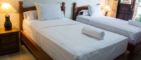 A hotel room with two single beds, wooden headboards, white linens, and bedside lamps.