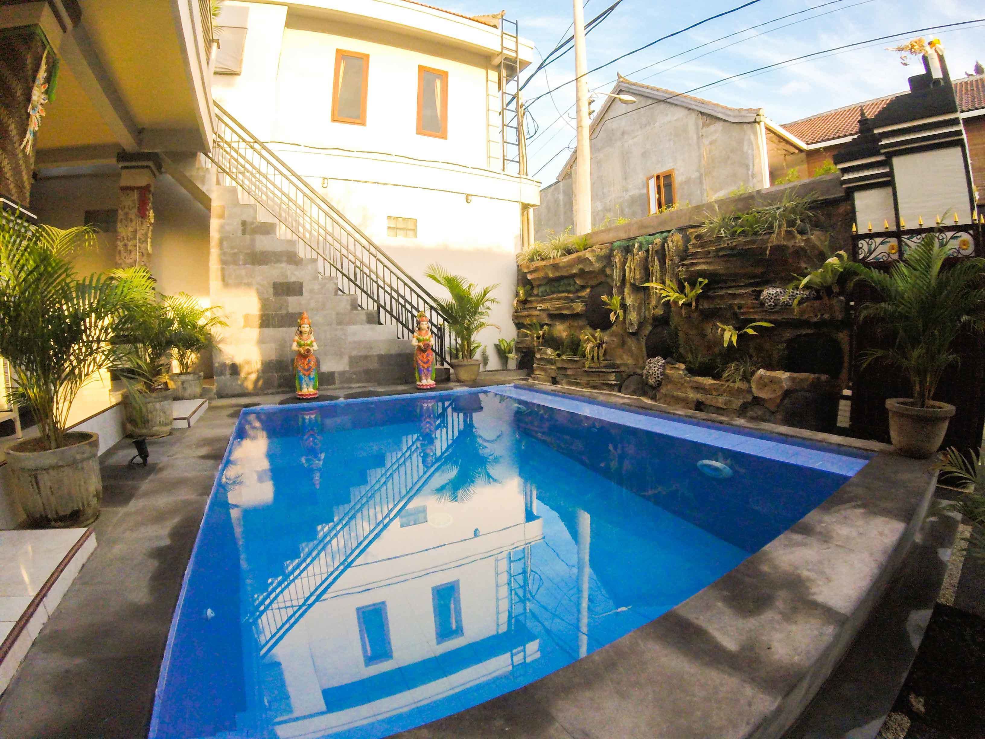 A swimming pool with a reflection of a building, surrounded by potted plants and a staircase leading to an upper level.