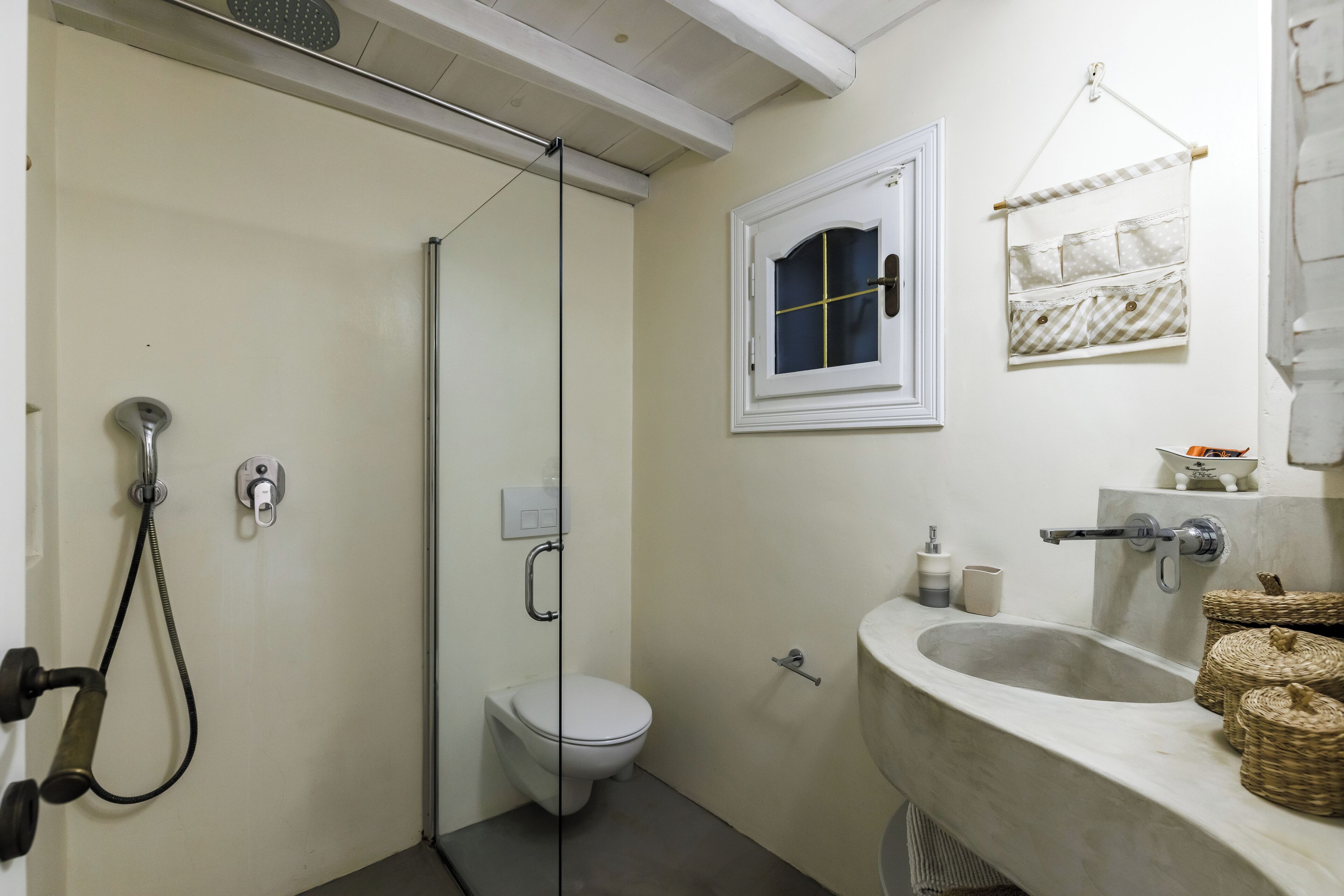 A bathroom with a shower, toilet, sink, and a small window.