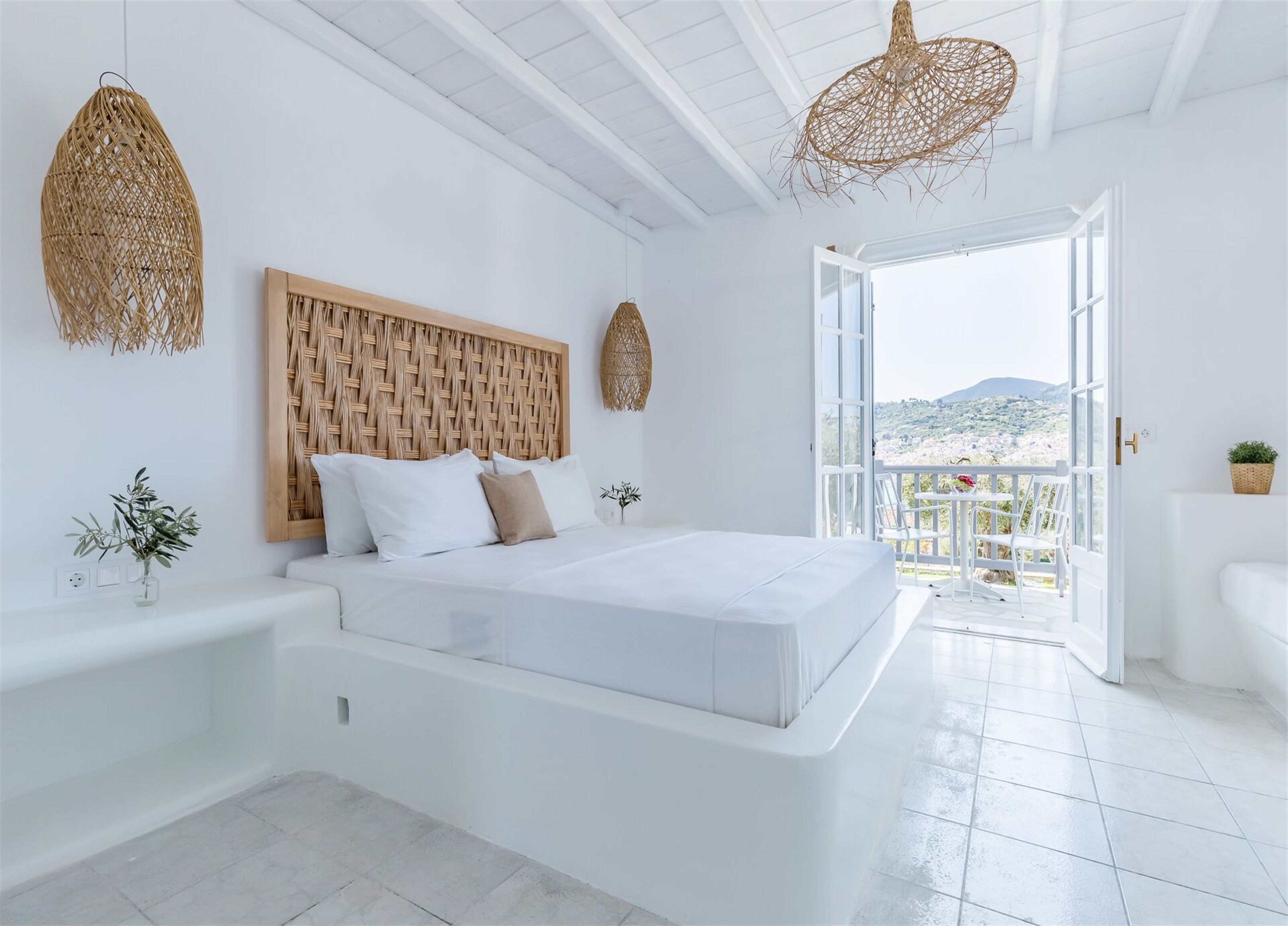 Une chambre moderne avec un grand lit, des murs blancs et une vue sur l’extérieur.