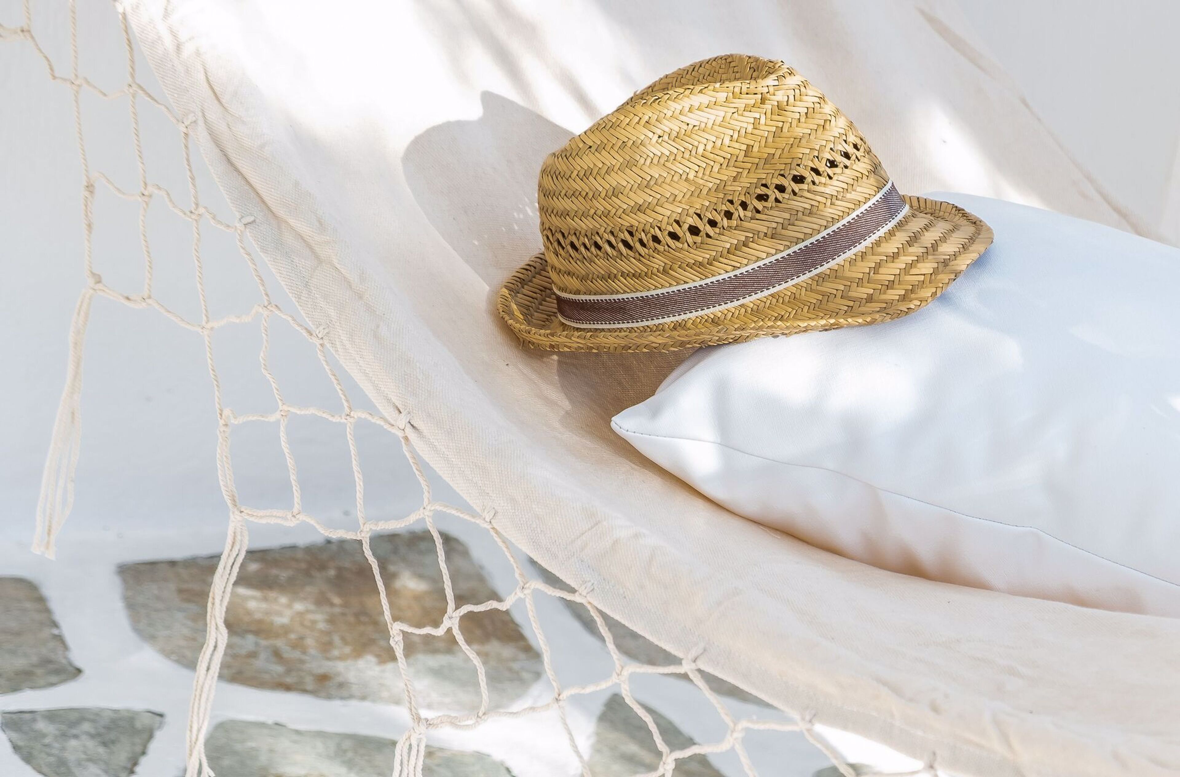 A straw hat on a white pillow in a hammock.