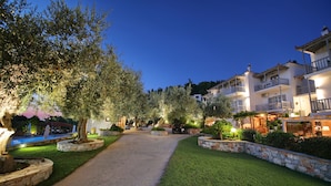 A well-lit pathway leading to a building with multiple balconies and a pool area visible in the background. - Evlalia Studios & Villas (Skopelos)