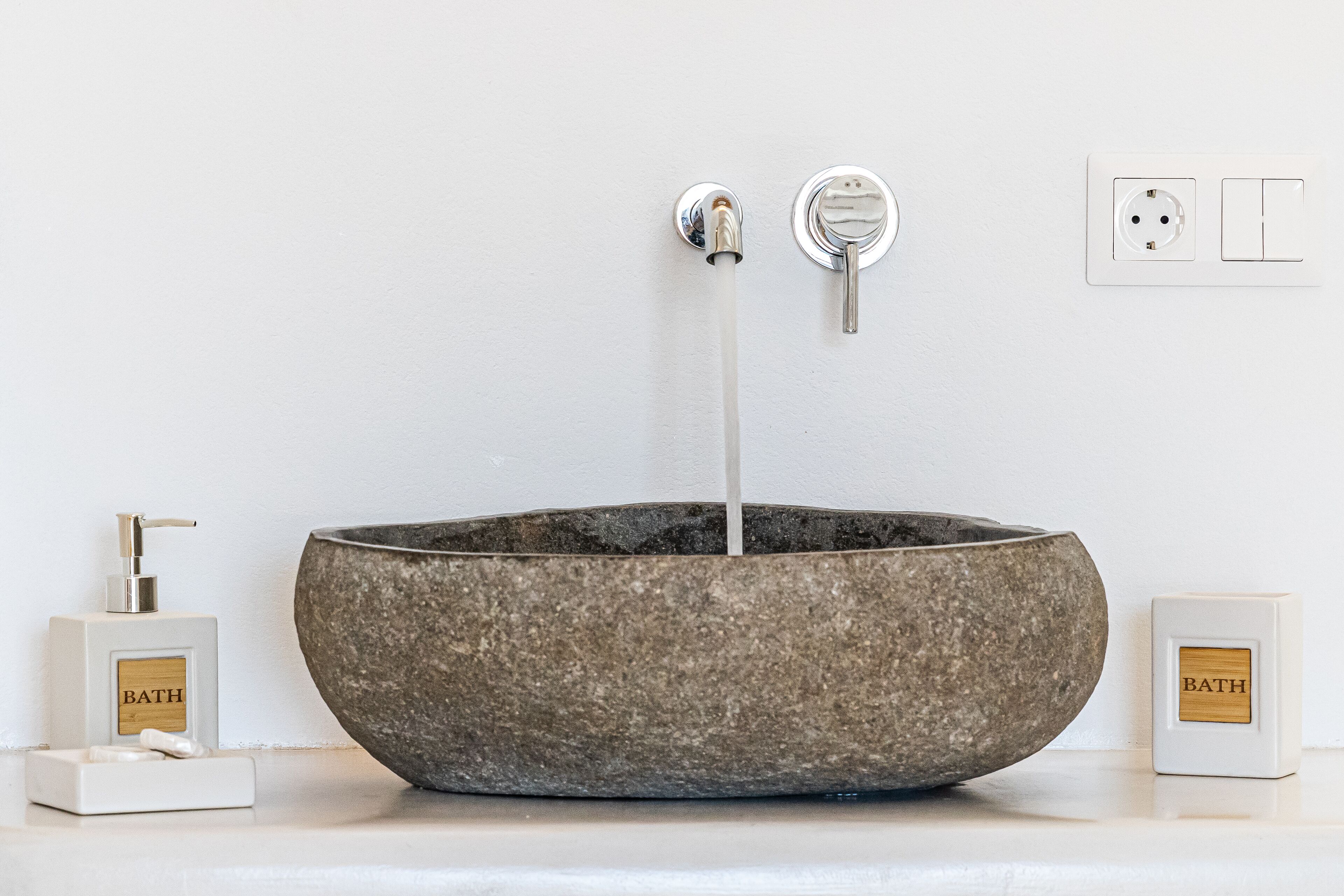 A bathroom with a stone sink, a soap dispenser, and a soap dish.