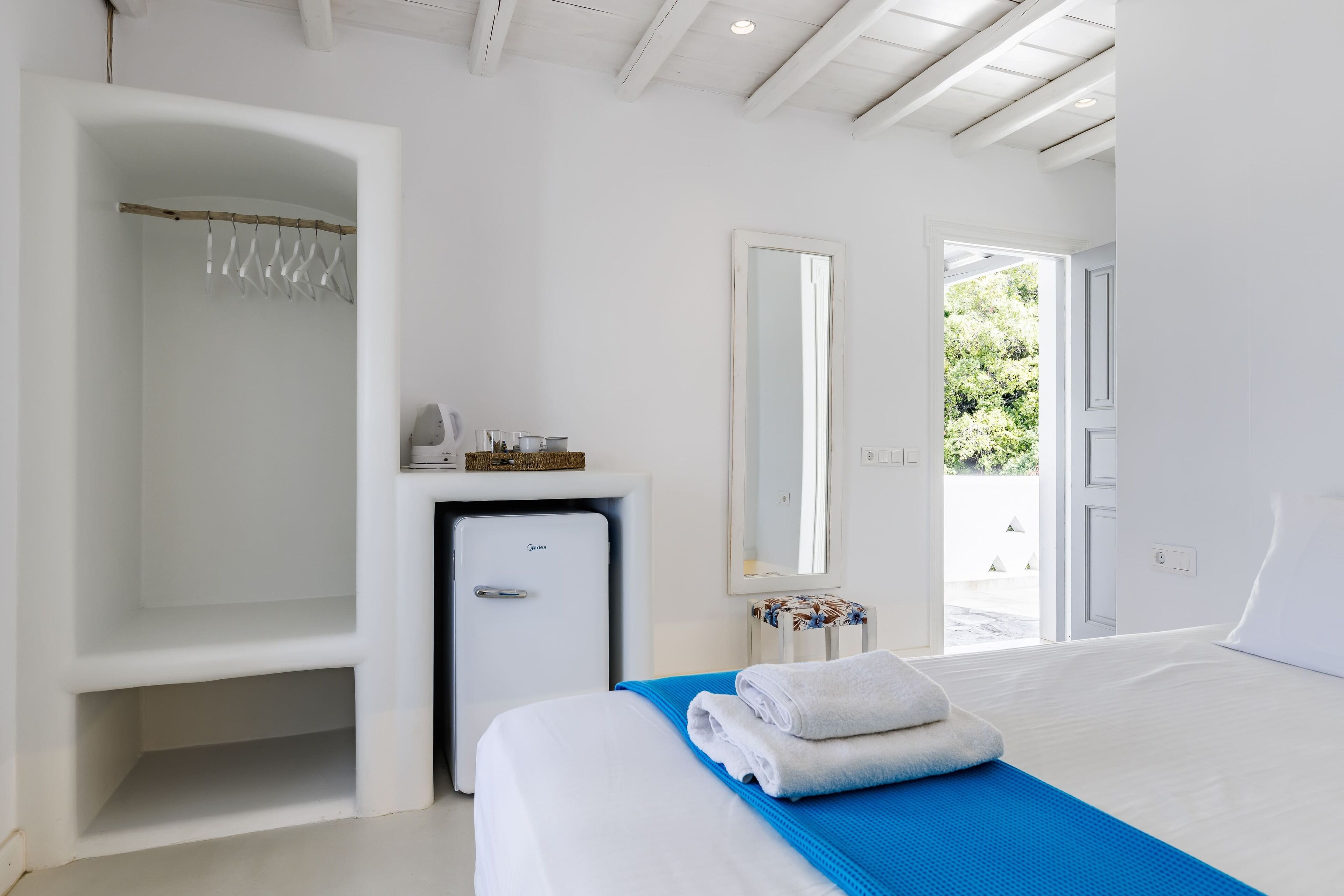 Une chambre d’hôtel comprenant un lit, un petit bureau avec un réfrigérateur, un porte-vêtements et un grand miroir.