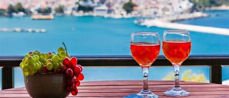 A wooden table with a bowl of fruit, two wine glasses, and a pair of sunglasses.