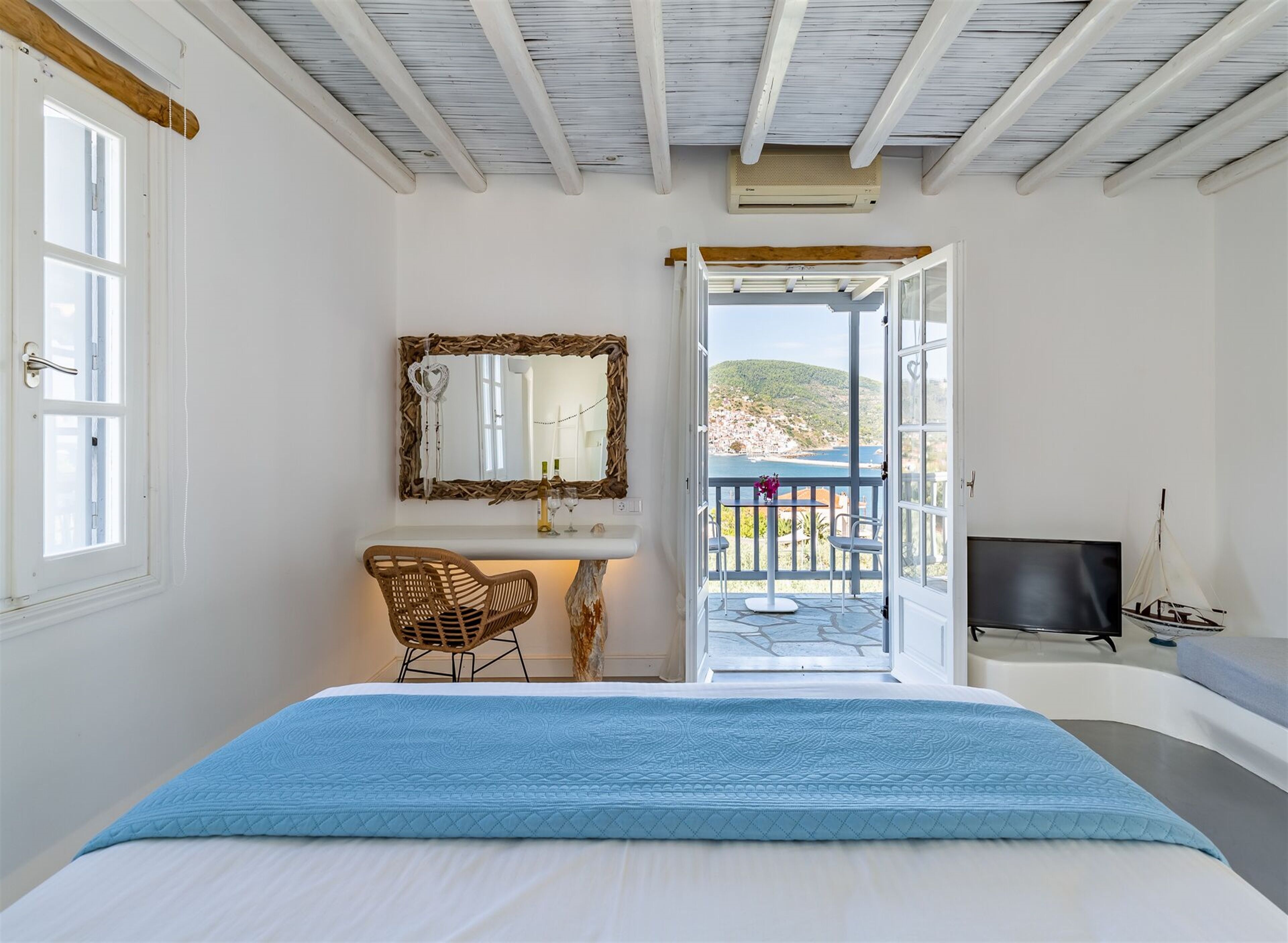 A bedroom with a bed, a dresser, a mirror, and a balcony with a TV and a sailboat model.