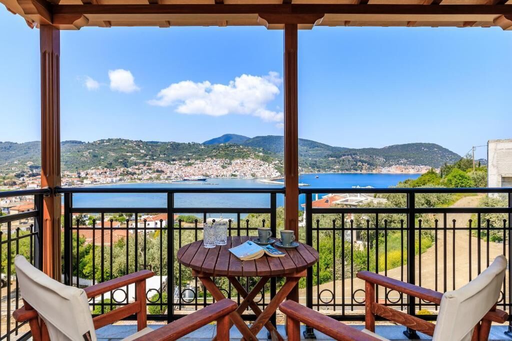 Een houten tafel met twee stoelen op een balkon met uitzicht op een kustplaats en een wateroppervlak.