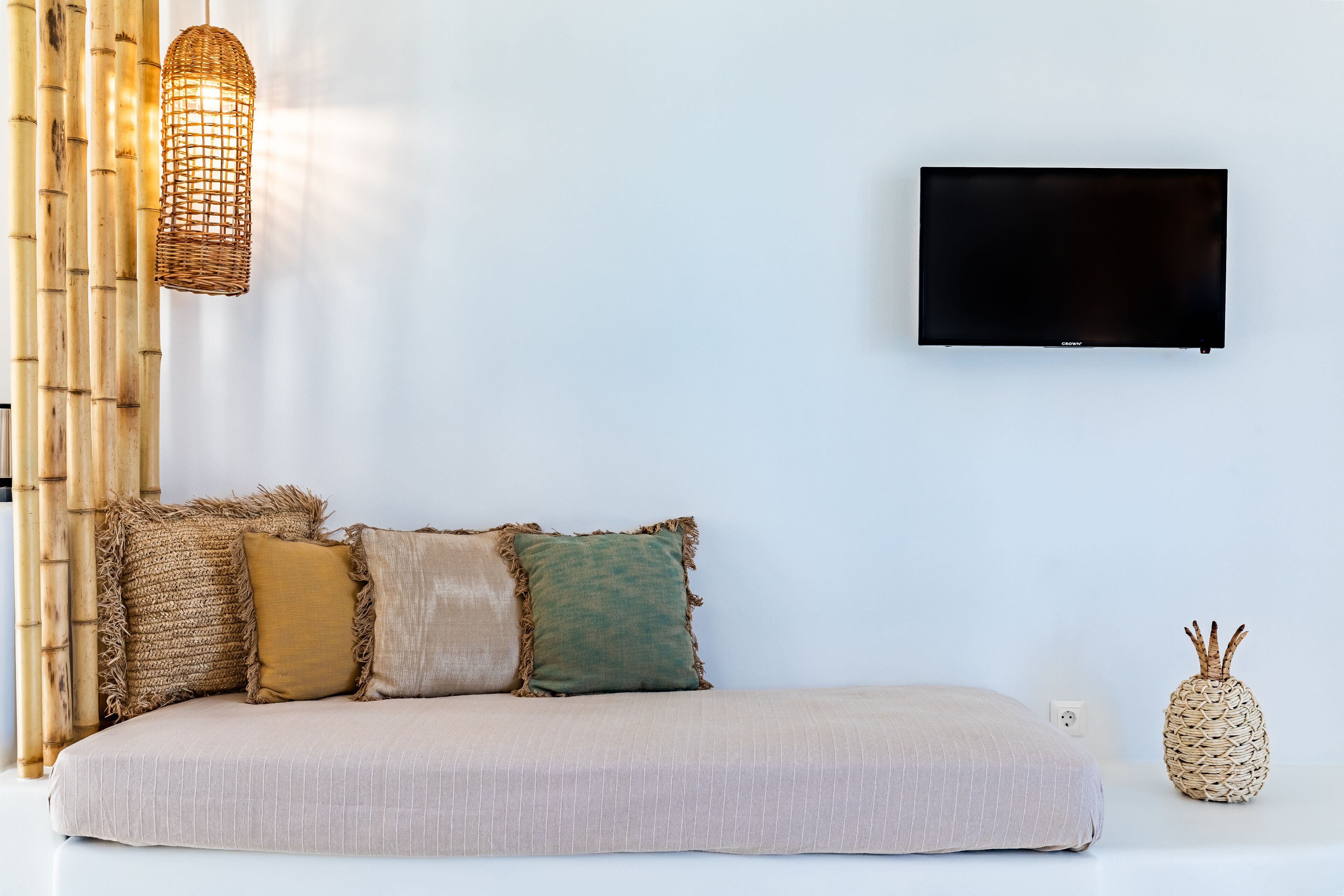 A modern living room with a sofa, a flat-screen TV, a woven light fixture, and a pineapple-shaped vase.