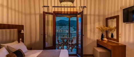 A hotel room with a bed, a desk, a chair, a TV, and a balcony with a view.