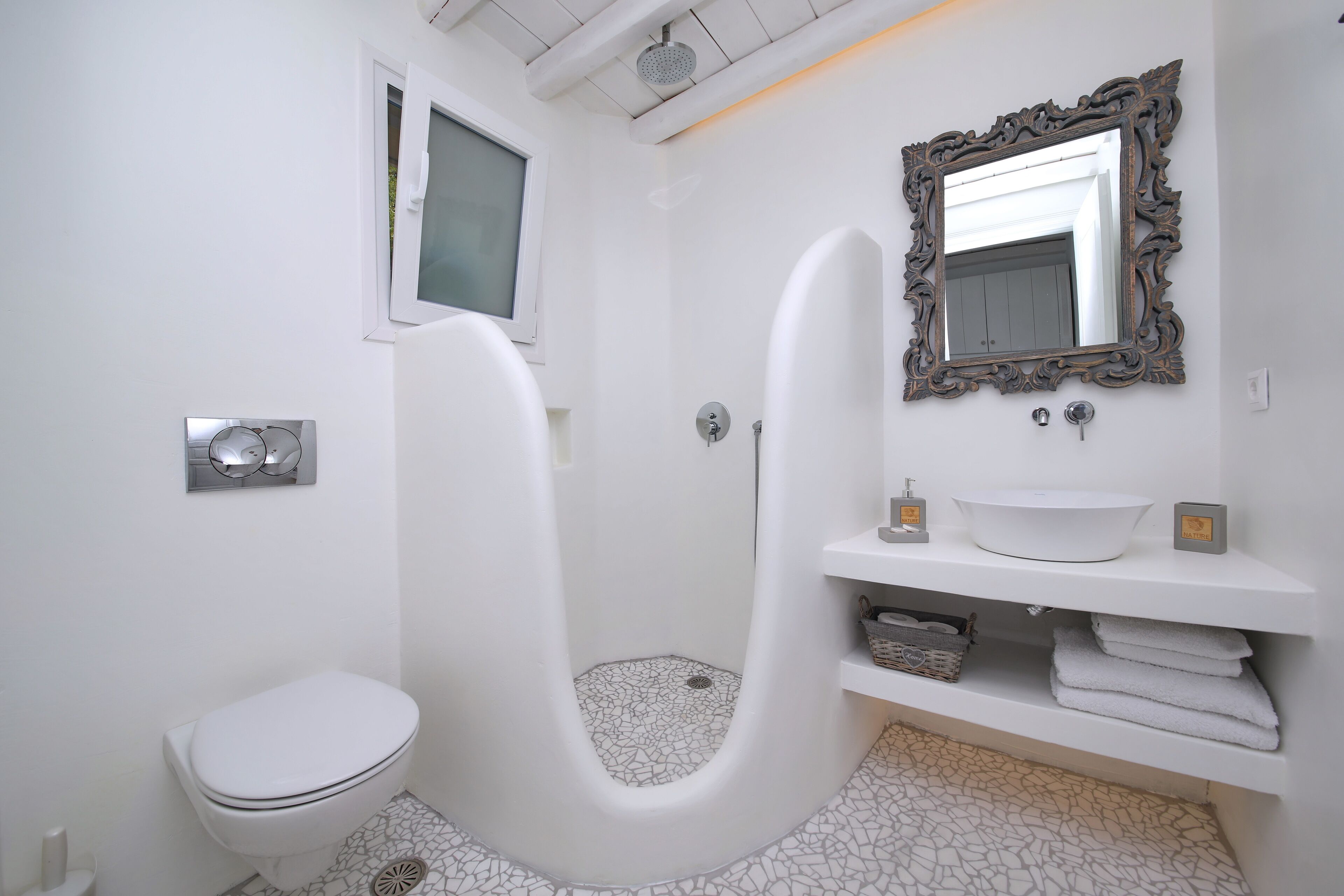A modern bathroom with a white toilet, a freestanding bathtub, a sink with a decorative mirror, and a showerhead.
