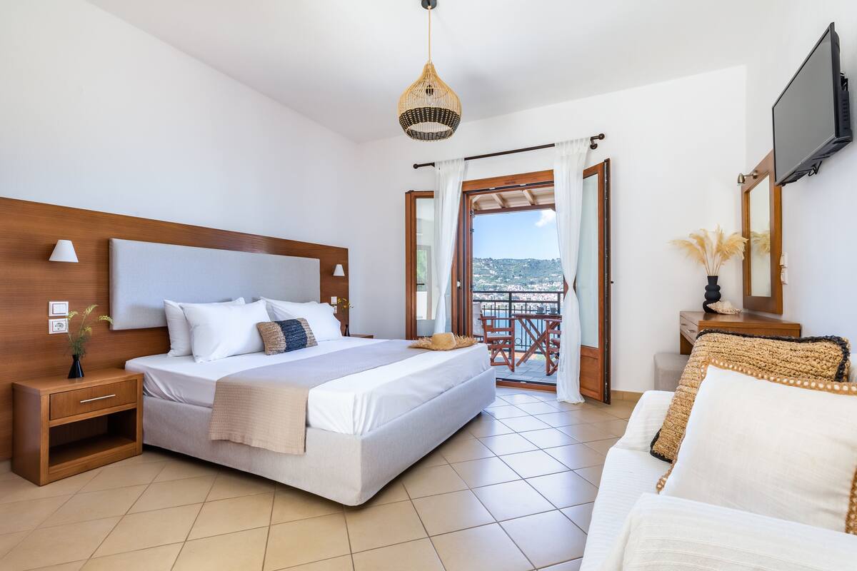 Une chambre dotée d’un grand lit, d’une tête de lit en bois, de tables de chevet, d’une télévision et d’un balcon avec vue.