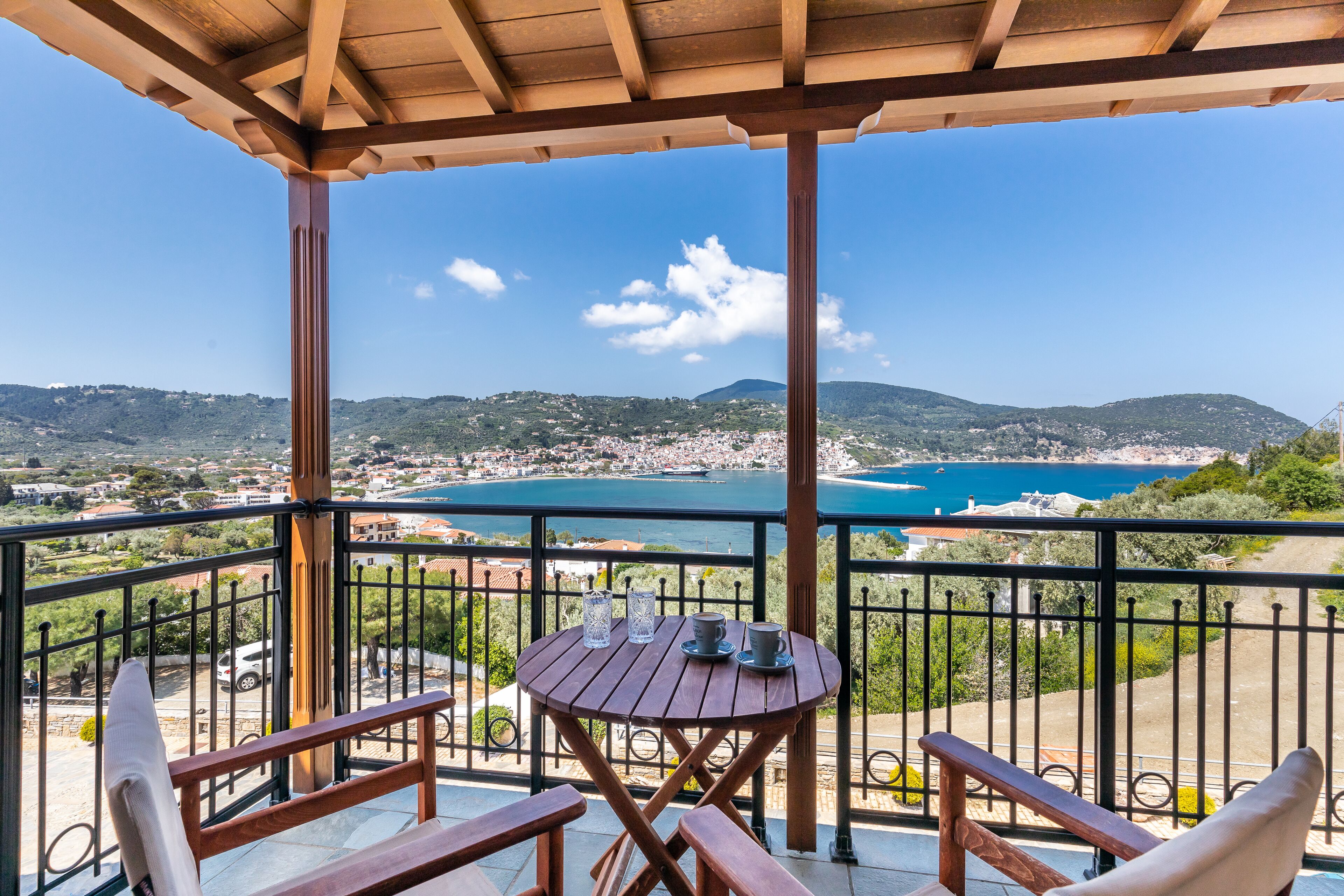 Une pergola en bois avec une table et des chaises, offrant une vue sur une ville côtière et la mer.