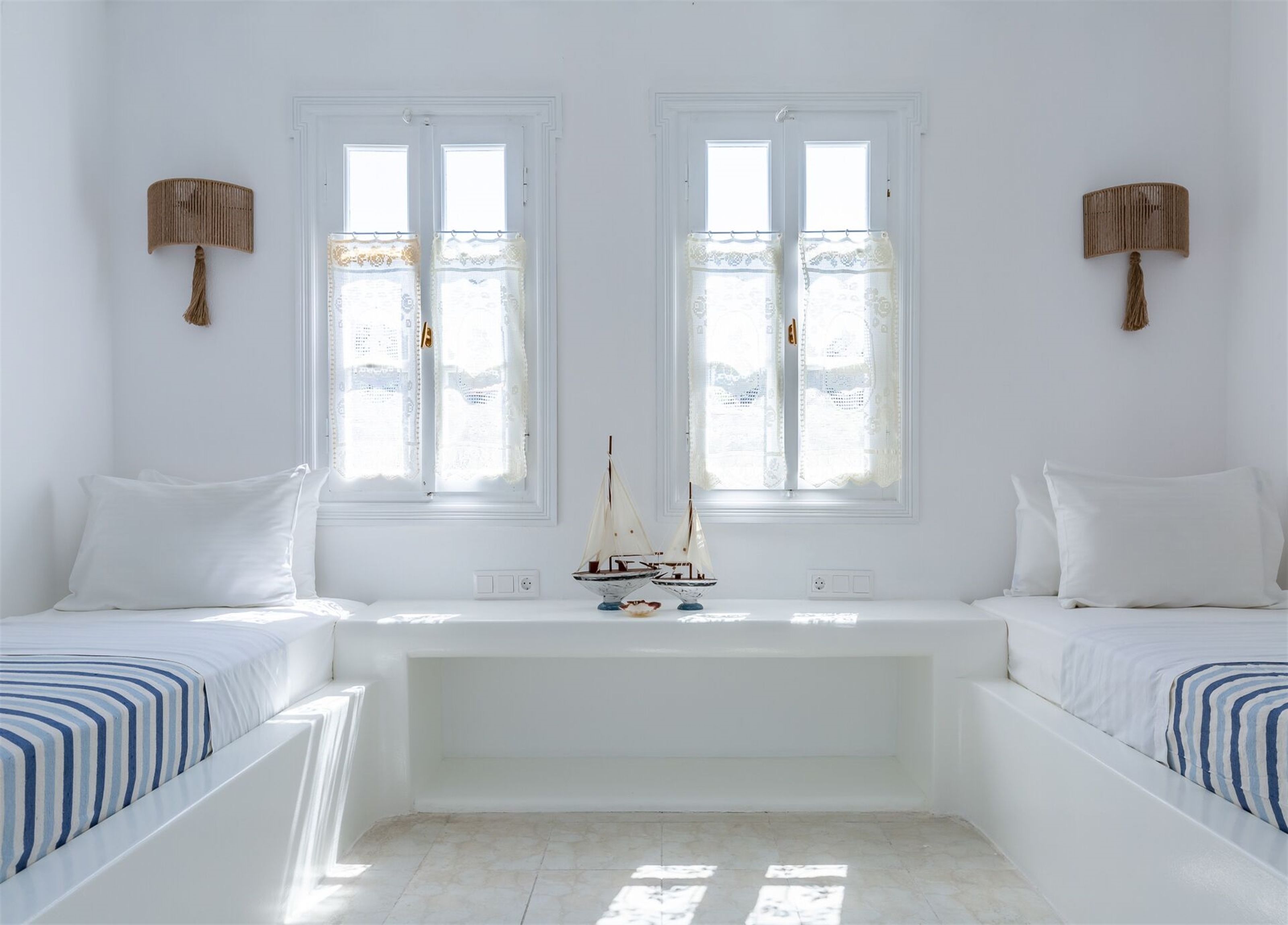 Una habitación con dos camas, una mesita y dos ventanas con cortinas.