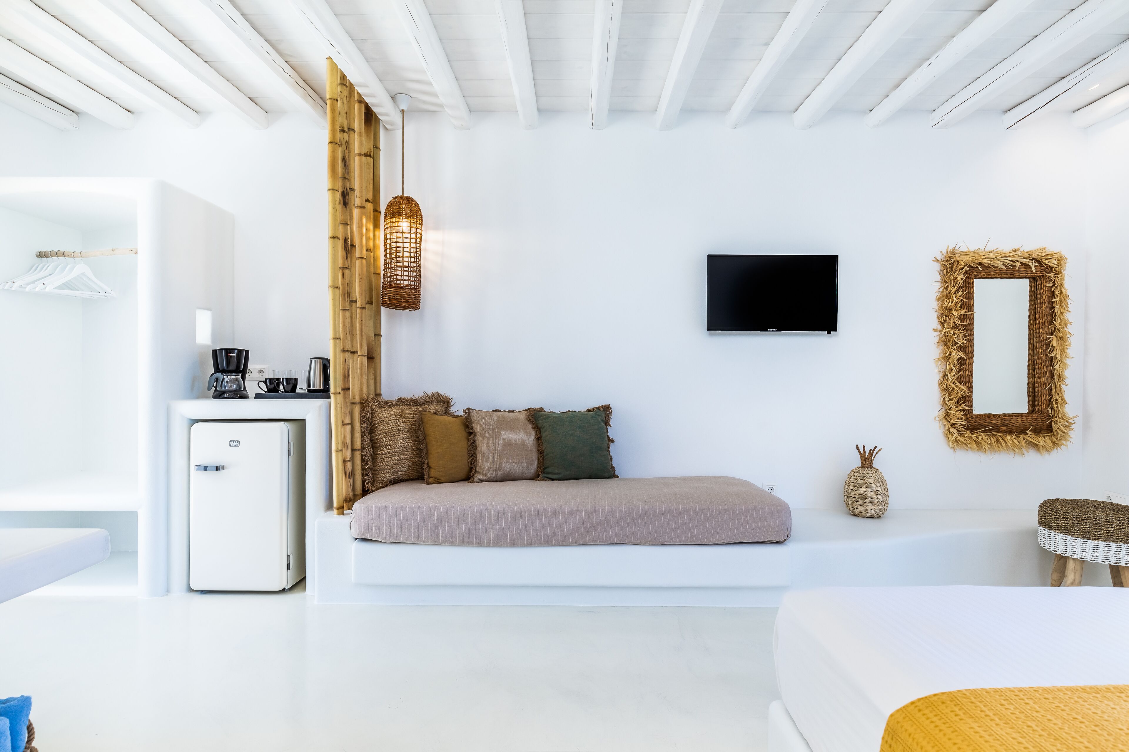Un dormitorio moderno y minimalista con sofá blanco, mesita de noche pequeña, televisión y espejo montado en la pared.