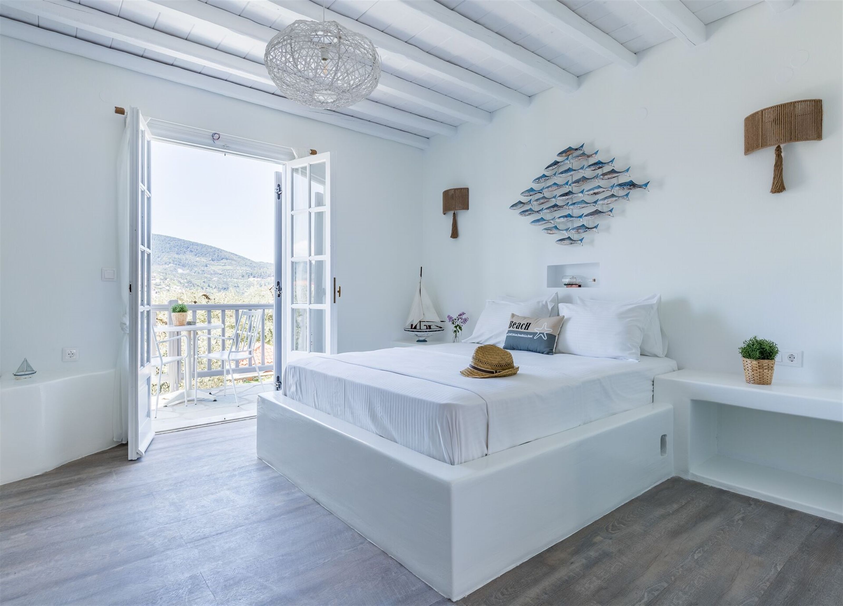 A spacious bedroom with a large bed, a balcony with a view, and a decorative wall piece.