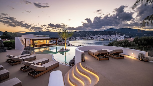 A rooftop pool area with lounge chairs, a bar, and a view of a coastal town at sunset. - Evlalia Studios & Villas (Skopelos)