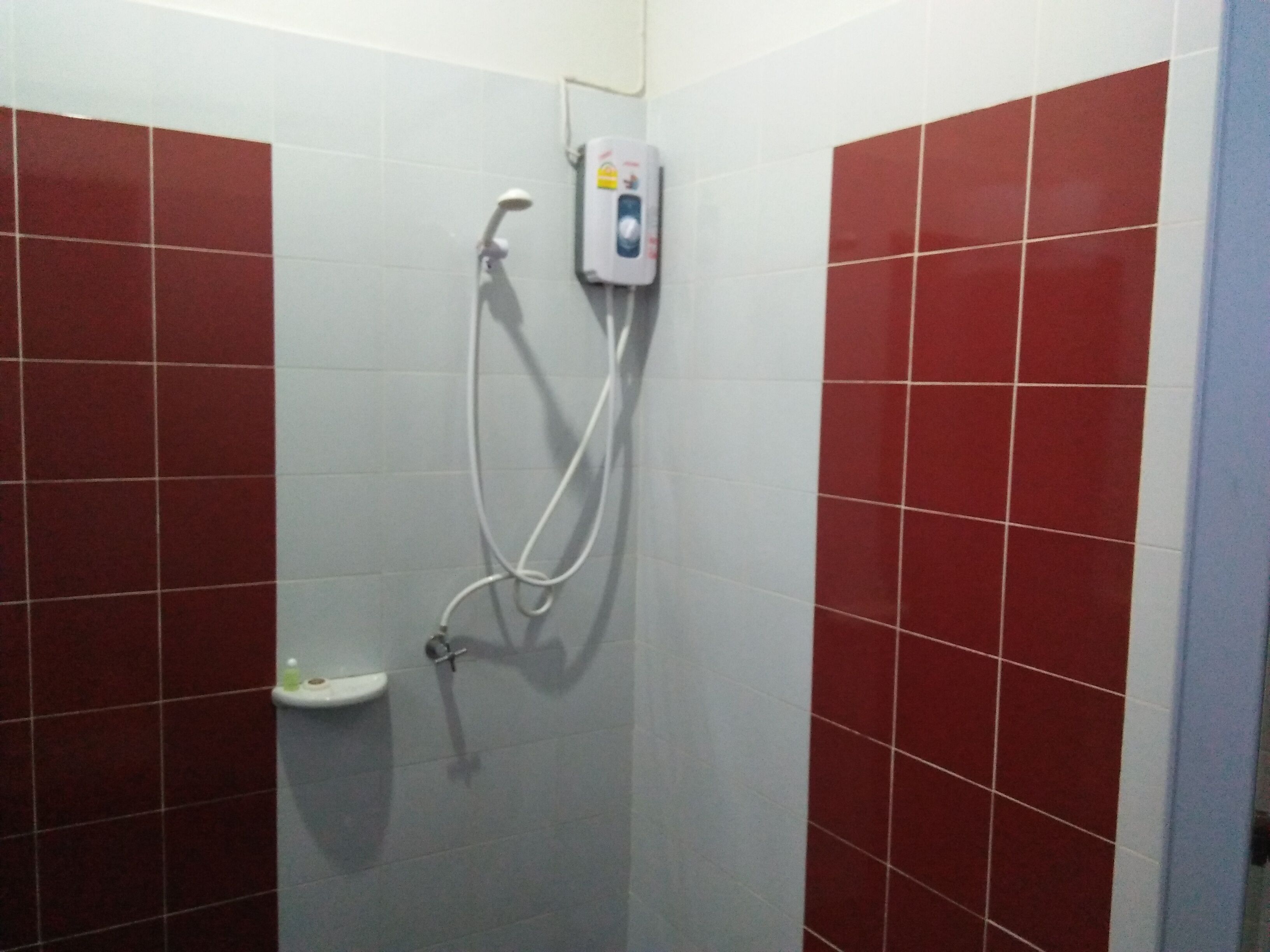 Una ducha con azulejos rojos y blancos, un cabezal de ducha manual y un dispensador de jabón.