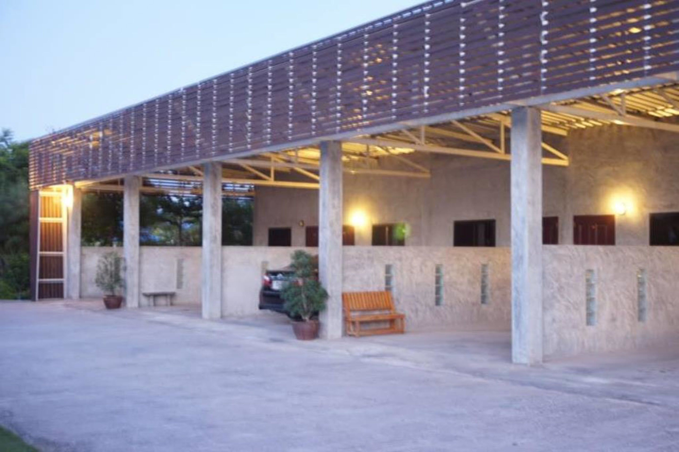 Un espacio al aire libre cubierto, con piso de concreto, columnas y un banco de madera.