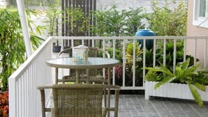 A balcony with a wicker table and chair, surrounded by potted plants and a view of greenery. - Sweet Mango Resort (Sung Noen)