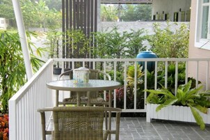 Varanda com mesa e cadeira de vime, cercada por plantas em vasos e vista para o verde.