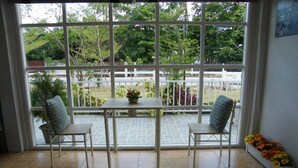 A room with a large window, two chairs, a table, and a potted plant. - Sweet Mango Resort (Sung Noen)