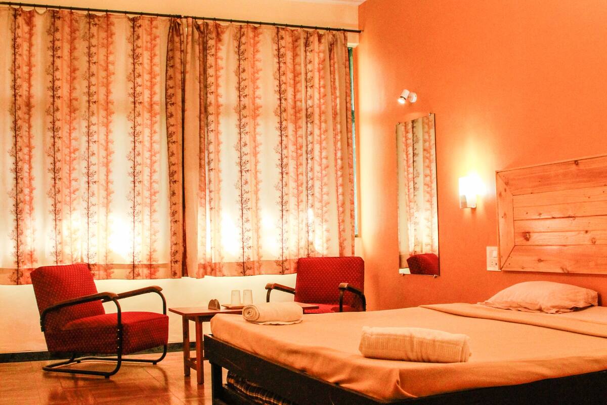Ein Hotelzimmer mit Bett, Schreibtisch, zwei Stühlen, Deckenventilator und Vorhängen.