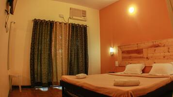 A hotel room with a bed, curtains, an air conditioning unit, and a wall-mounted light.
