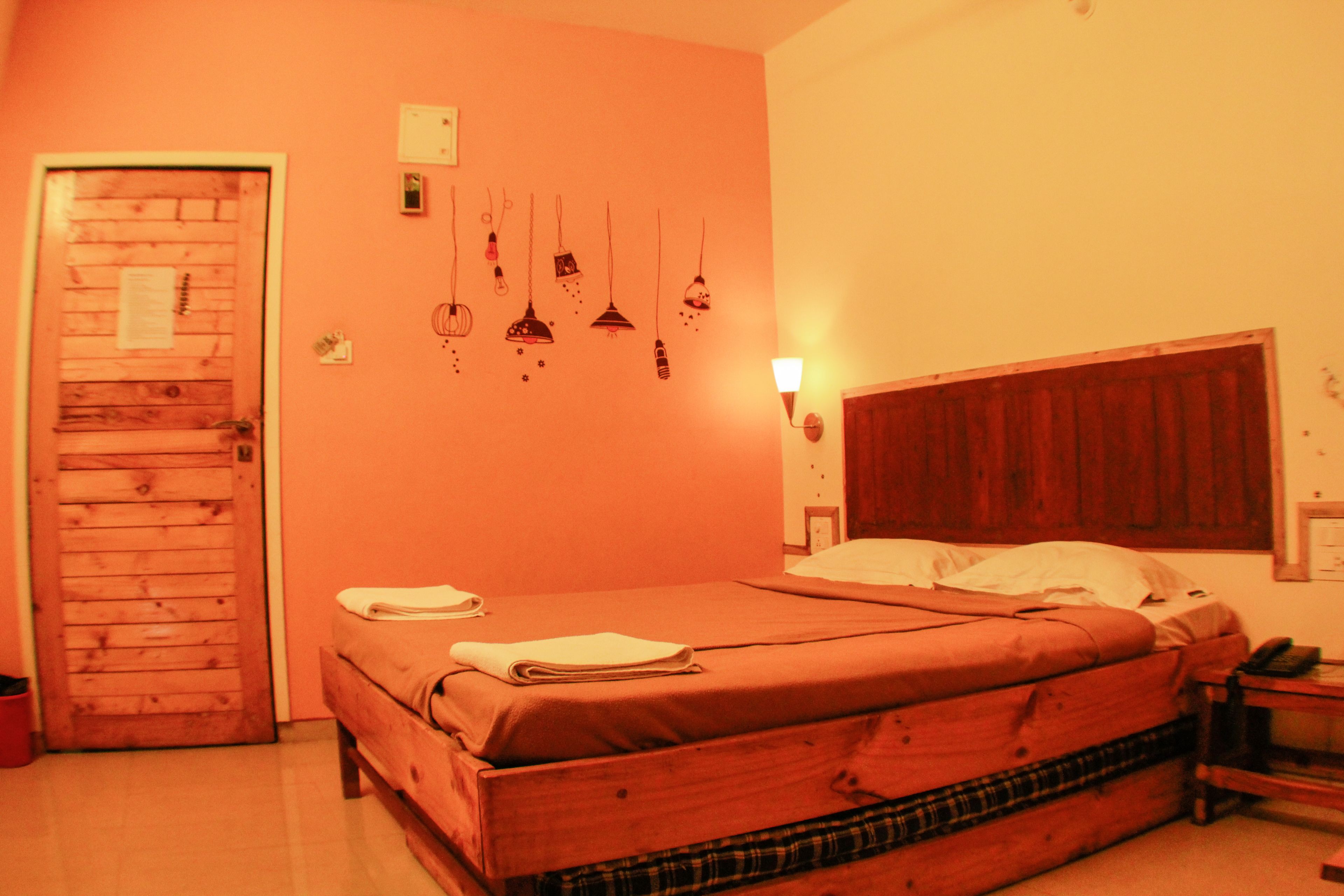 Une pièce avec un lit en bois, une porte en bois et un luminaire fixé au mur.