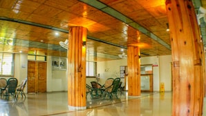 Un vestíbulo amplio con pilares de madera, un mostrador de recepción y un área de comedor con sillas.