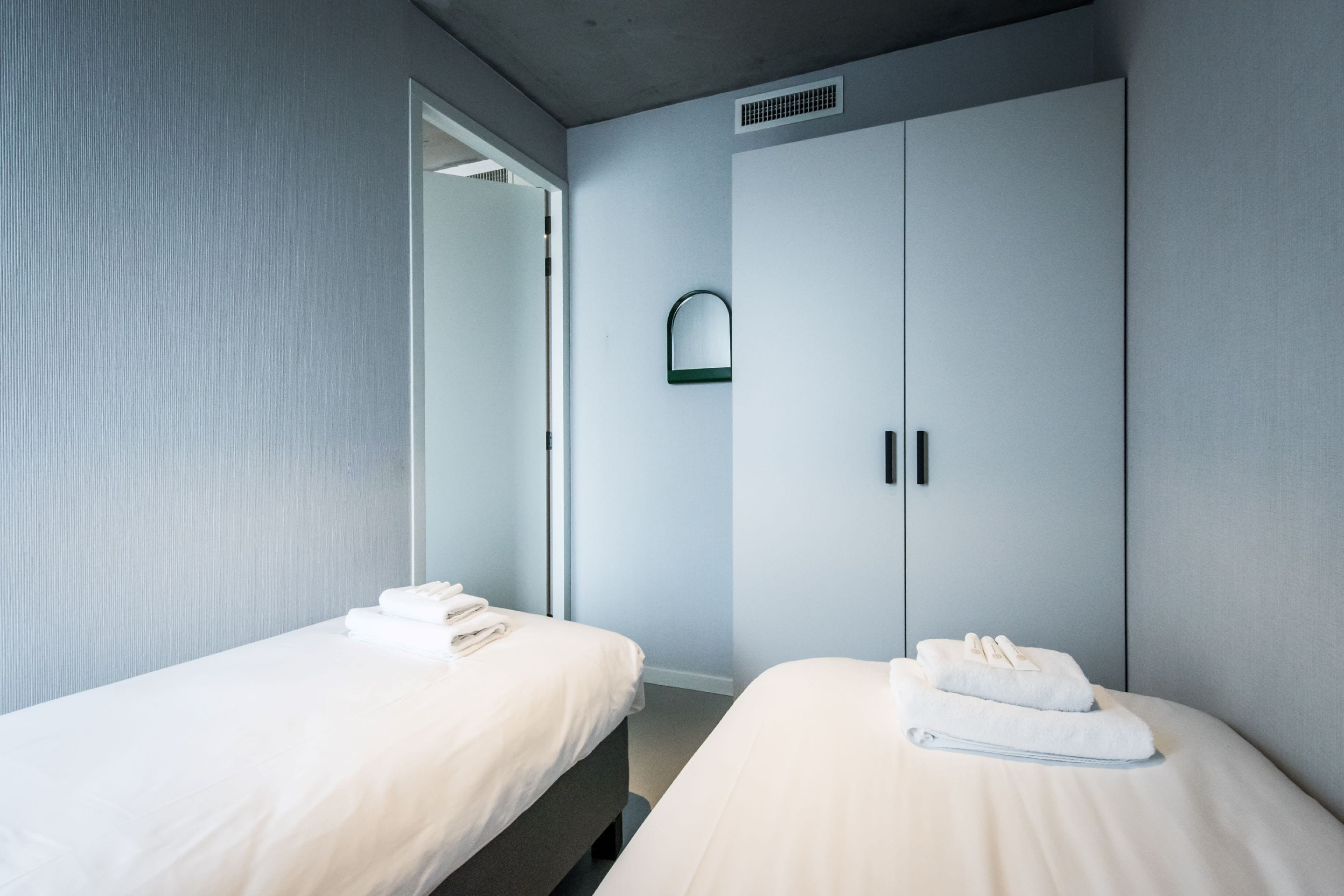 A hotel room with two beds, a wardrobe, and a mirror.