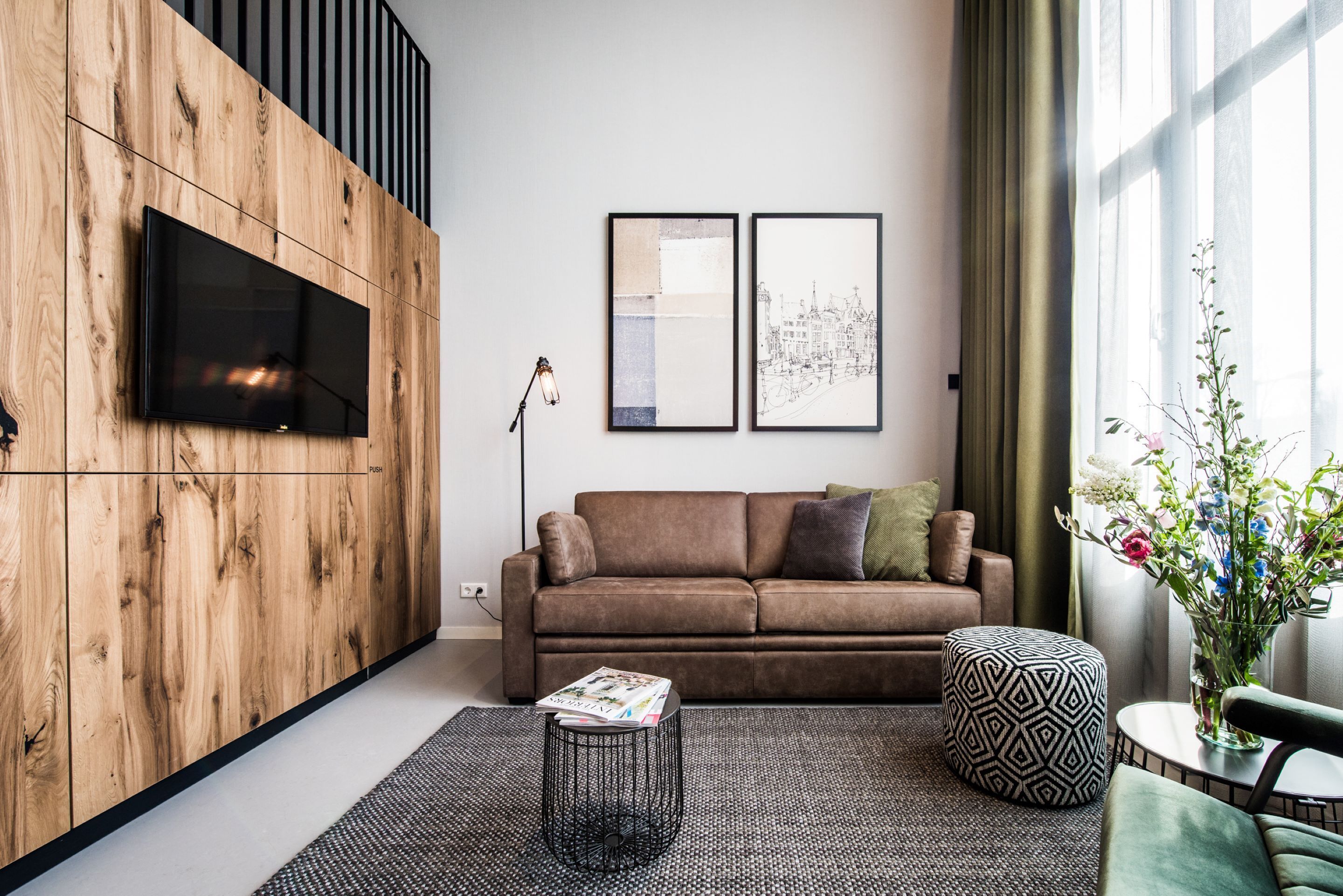 Un soggiorno moderno con una parete decorata in legno, una televisione a schermo piatto, un divano marrone, un poggiapiedi fantasia e un piccolo tavolino con una rivista.