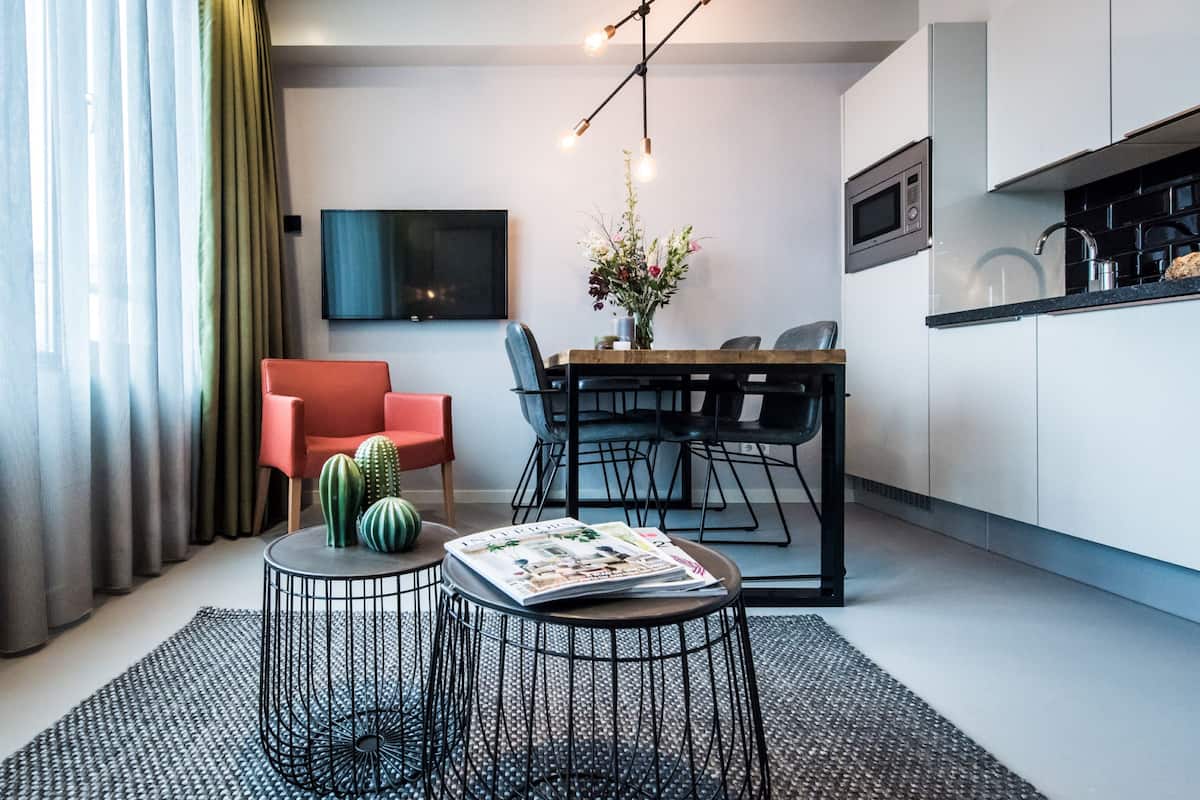 Ein modernes Wohnzimmer mit Essbereich, einem wandmontierten Flachbildfernseher und einer Küche mit weißen Schränken und einer schwarzen Arbeitsplatte.