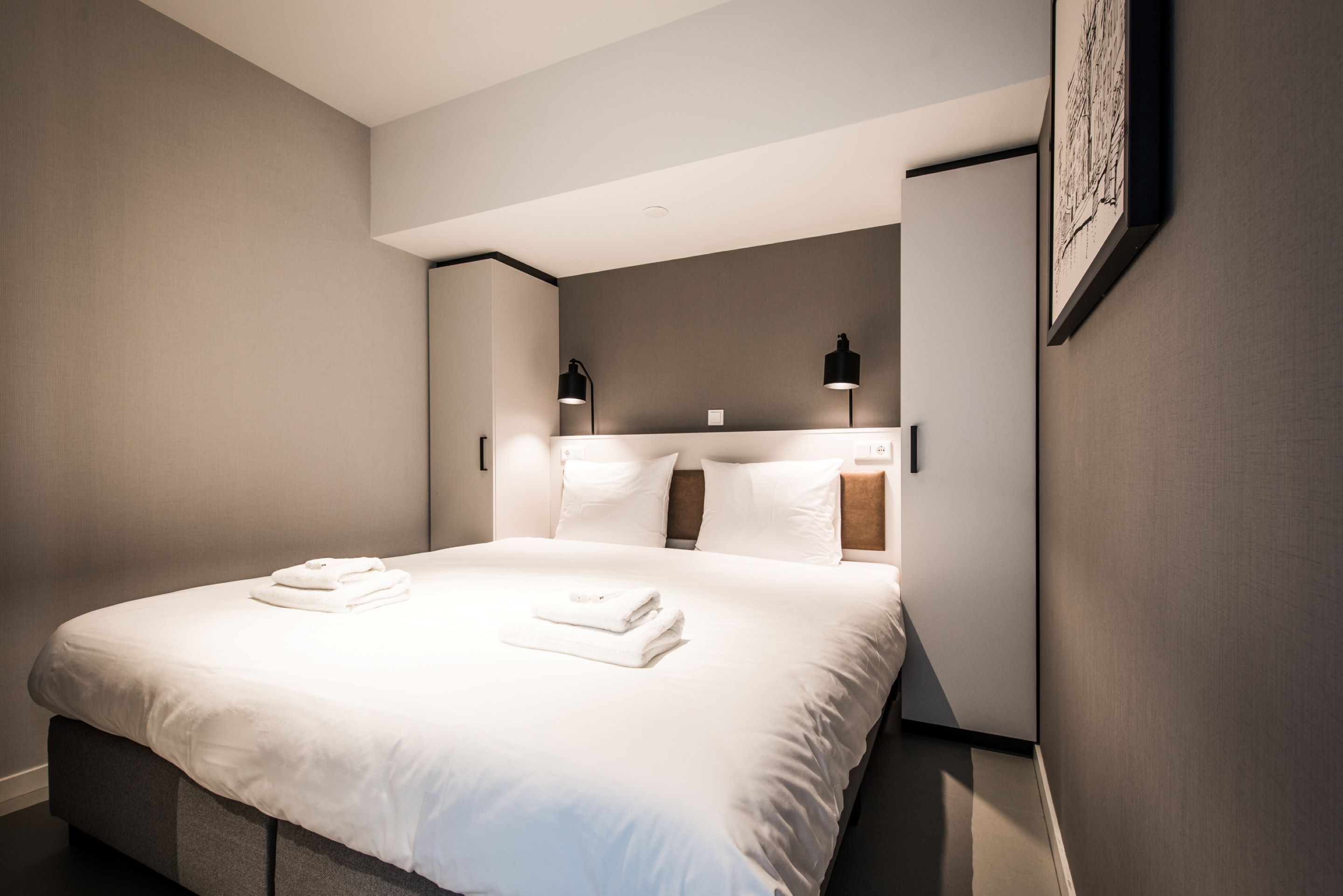 A modern hotel room with a large bed, two bedside lamps, and a framed artwork on the wall.