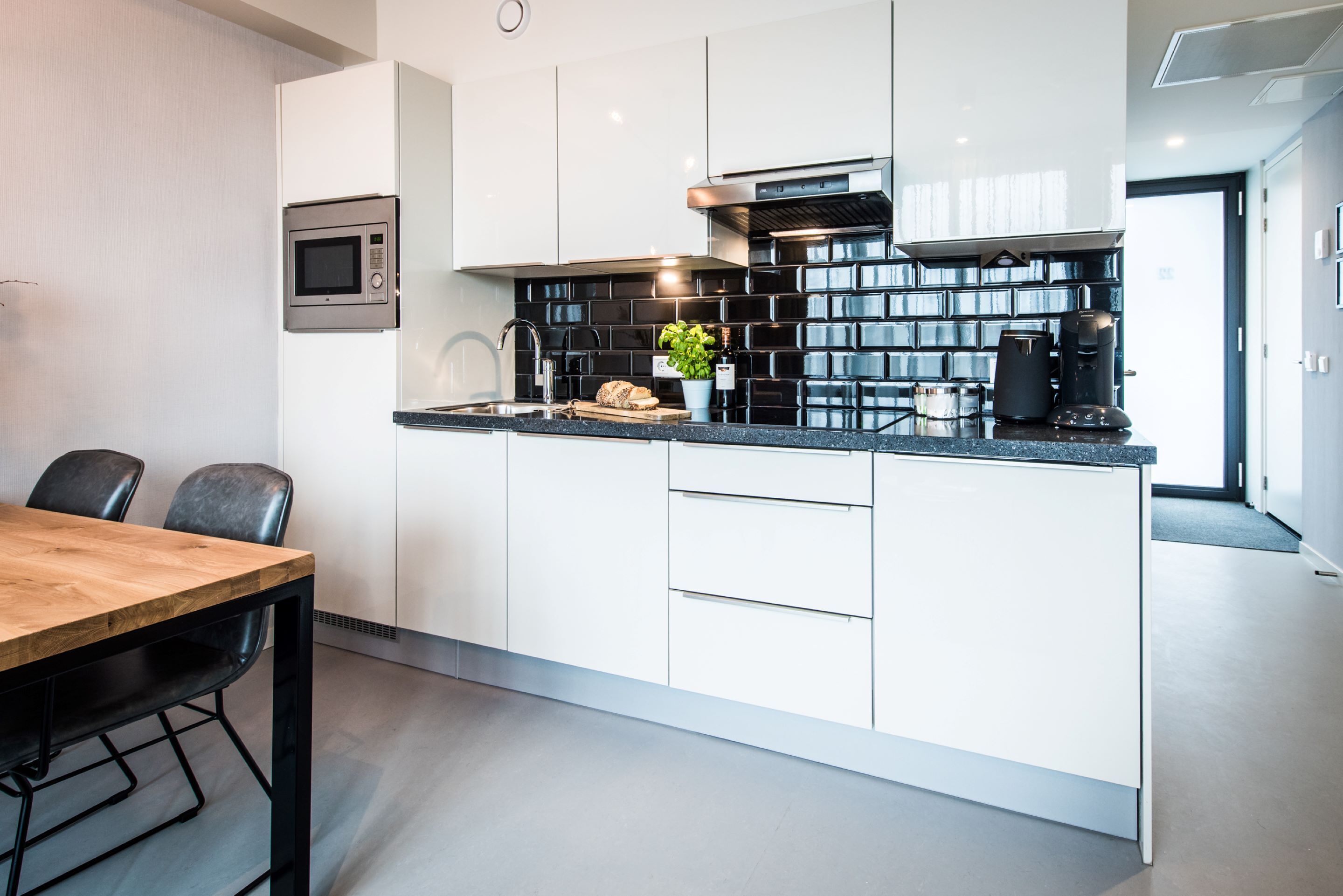 Een moderne keuken met witte kasten, een zwart aanrecht, een magnetron en een koffiezetapparaat.