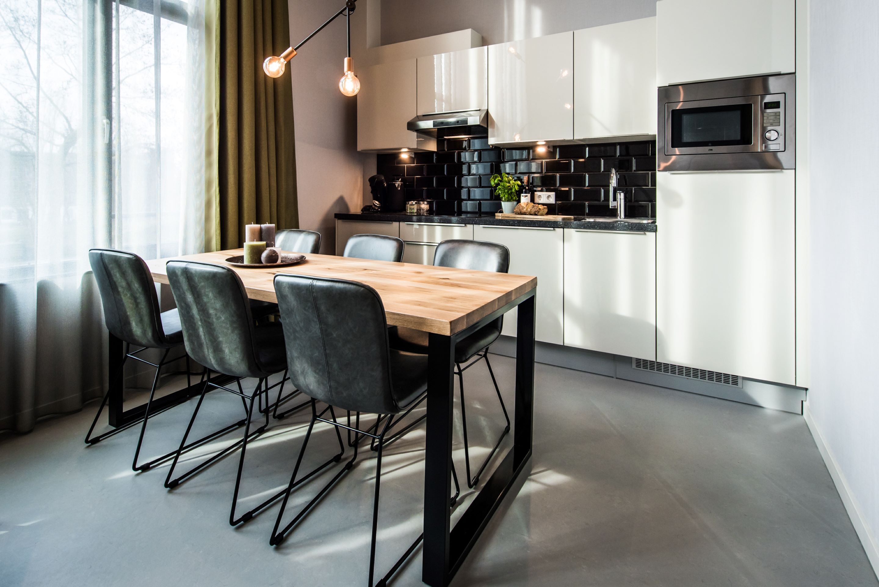 A modern kitchen with a dining area, featuring a wooden table, black chairs, and a built-in microwave.