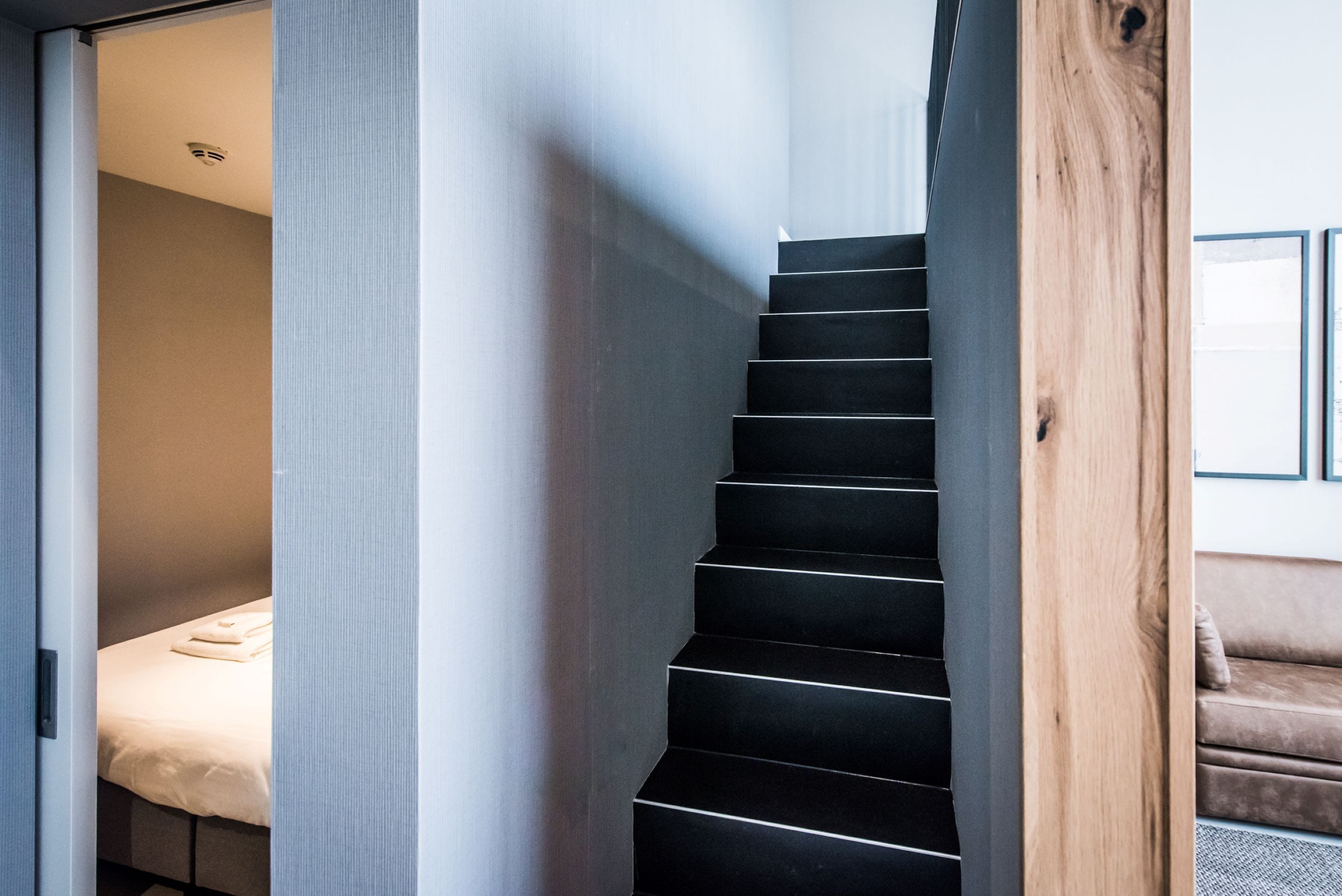 Een moderne trap met zwarte treden, een houten leuning en een beige muur.