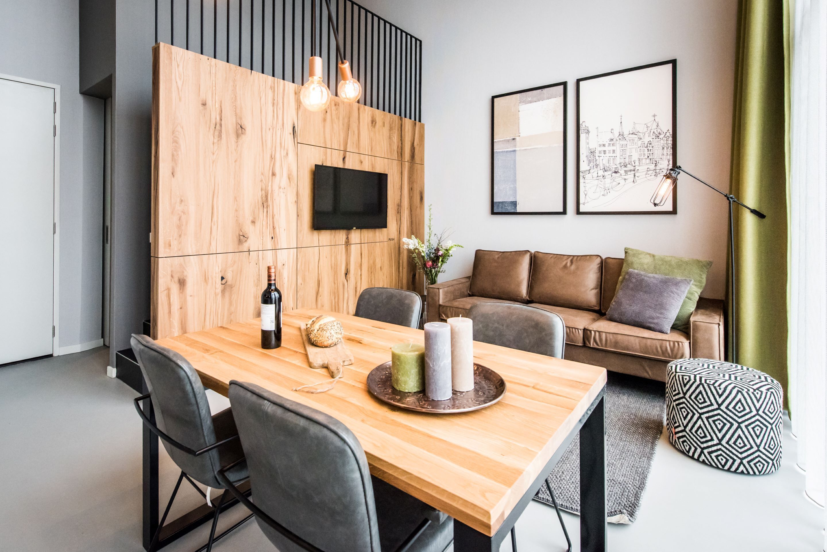 Ein modernes Wohnzimmer mit Esstisch aus Holz, Ledersofa und Fernseher, der an einer Holzwand angebracht ist.