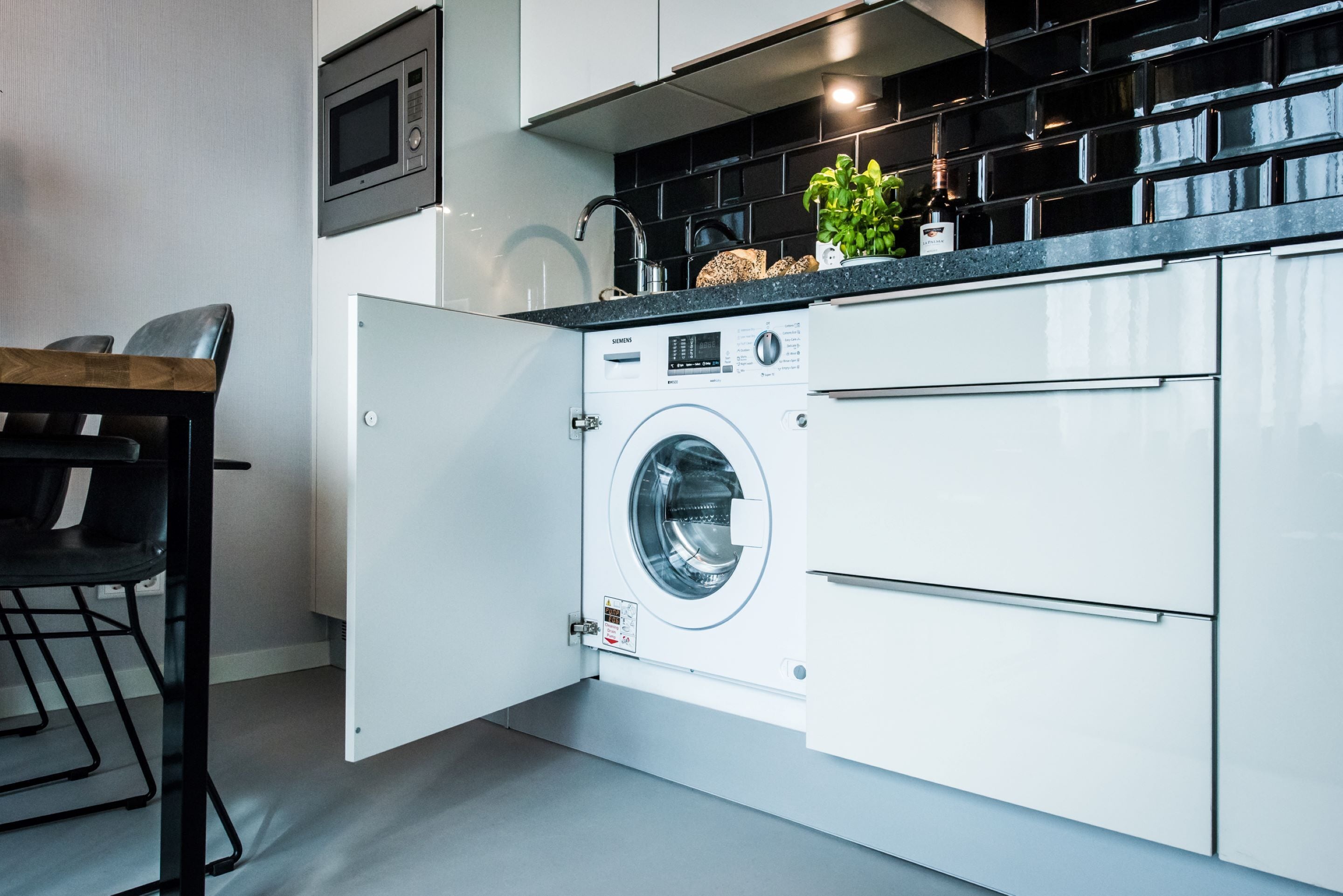 Une cuisine moderne dotée d’un lave-linge et d’un sèche-linge intégrés, d’un four à micro-ondes et d’un pare-feu noir.