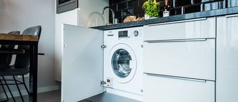 Une cuisine moderne dotée d’un lave-linge et d’un sèche-linge intégrés, d’un four à micro-ondes et d’un pare-feu noir.