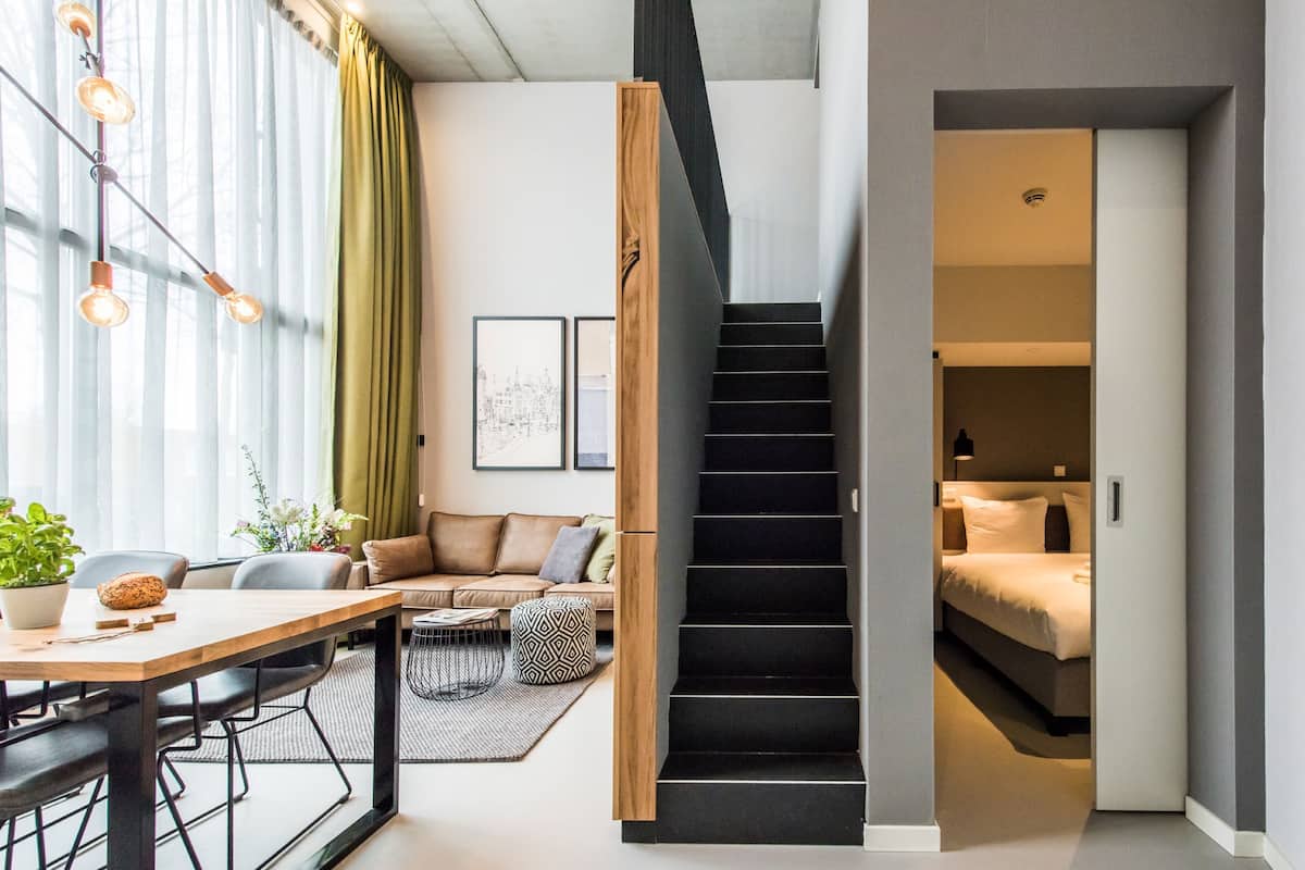 Ein modernes Interieur mit einer Treppe zu einem Schlafzimmer, einem Essbereich mit Tisch und Stühlen sowie einem Wohnbereich mit Sofa und Couchtisch.