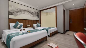 Two single beds with matching headboards, a large abstract artwork, and a comfortable seating area.