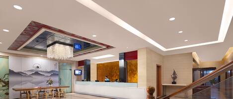 A modern hotel lobby with a reception desk, seating area, and a staircase.
