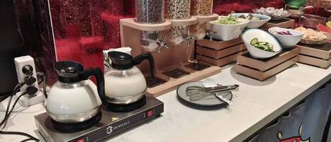 Un plan de travail de cuisine avec deux bouilloires électriques, une machine à café et divers récipients pour aliments.