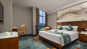 A hotel room with a large bed, a desk with a chair, a window with curtains, and a painting on the wall. - Kaiserdom Hotel Airport Branch (Guangzhou)