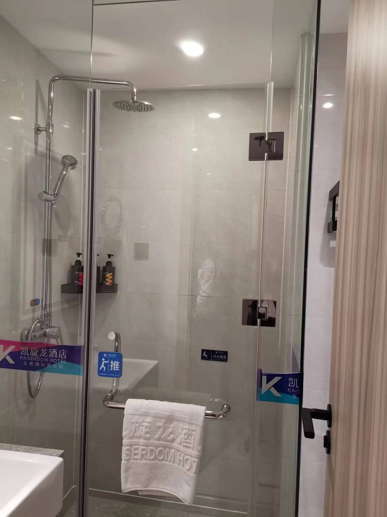 A modern bathroom with a glass-enclosed shower, a visible towel rack with a towel, and a sink area.
