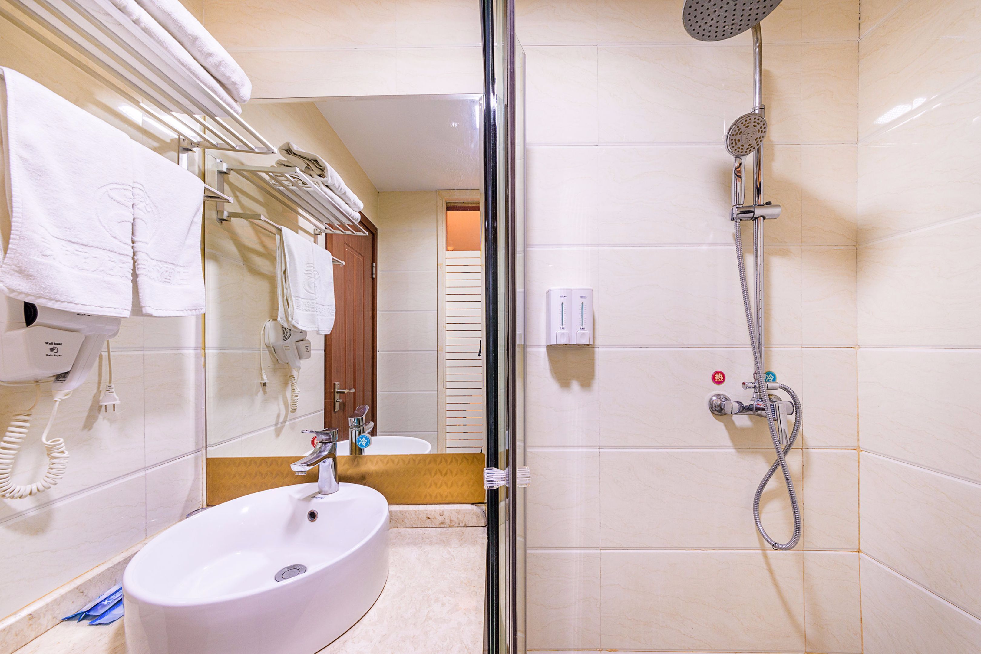 A hotel bathroom with a sink, mirror, towel rack, shower, and toilet.
