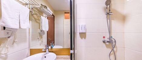 A hotel bathroom with a sink, mirror, towel rack, shower, and toilet.