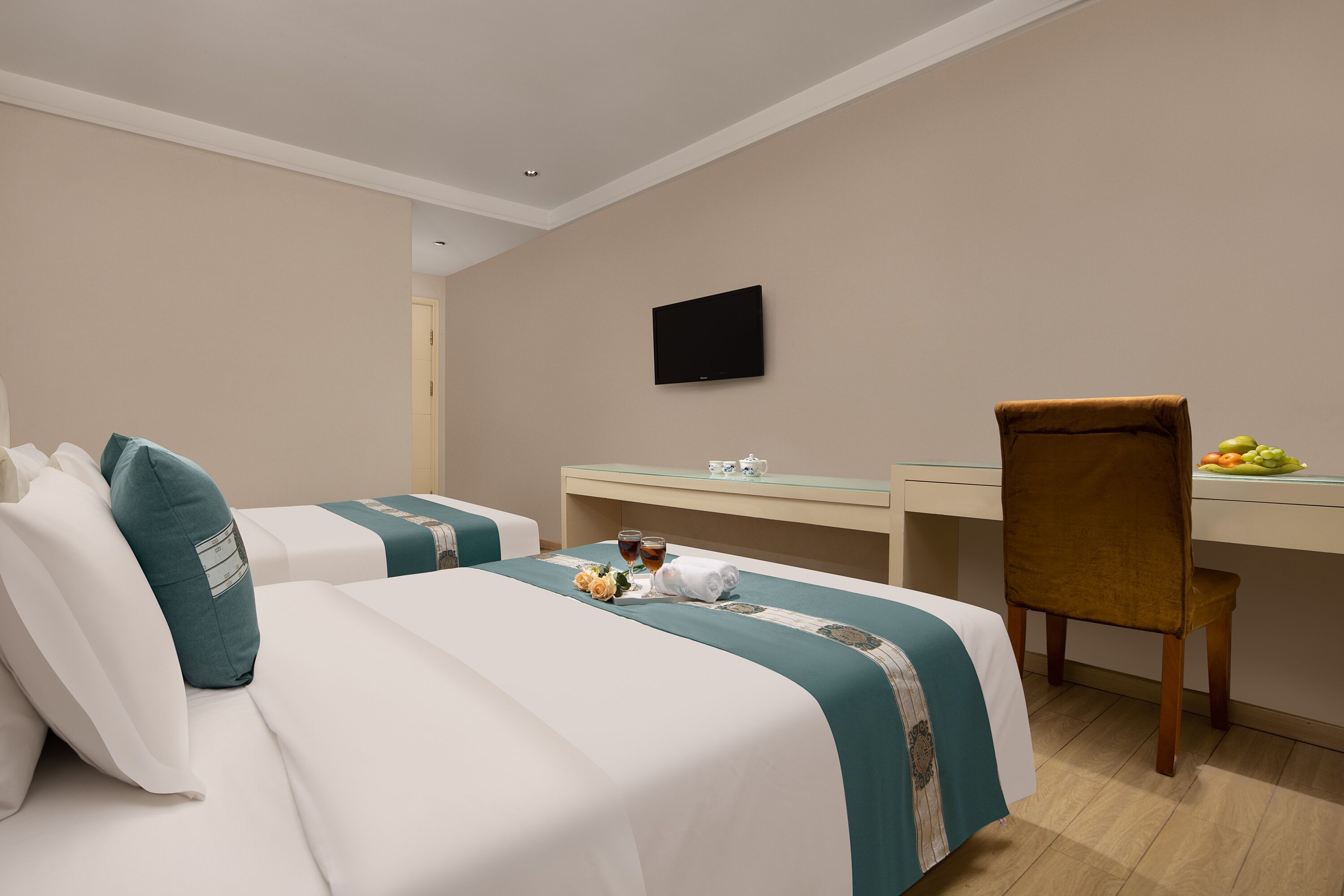 Una habitación de hotel con dos camas, un escritorio, una silla y un televisor en la pared.